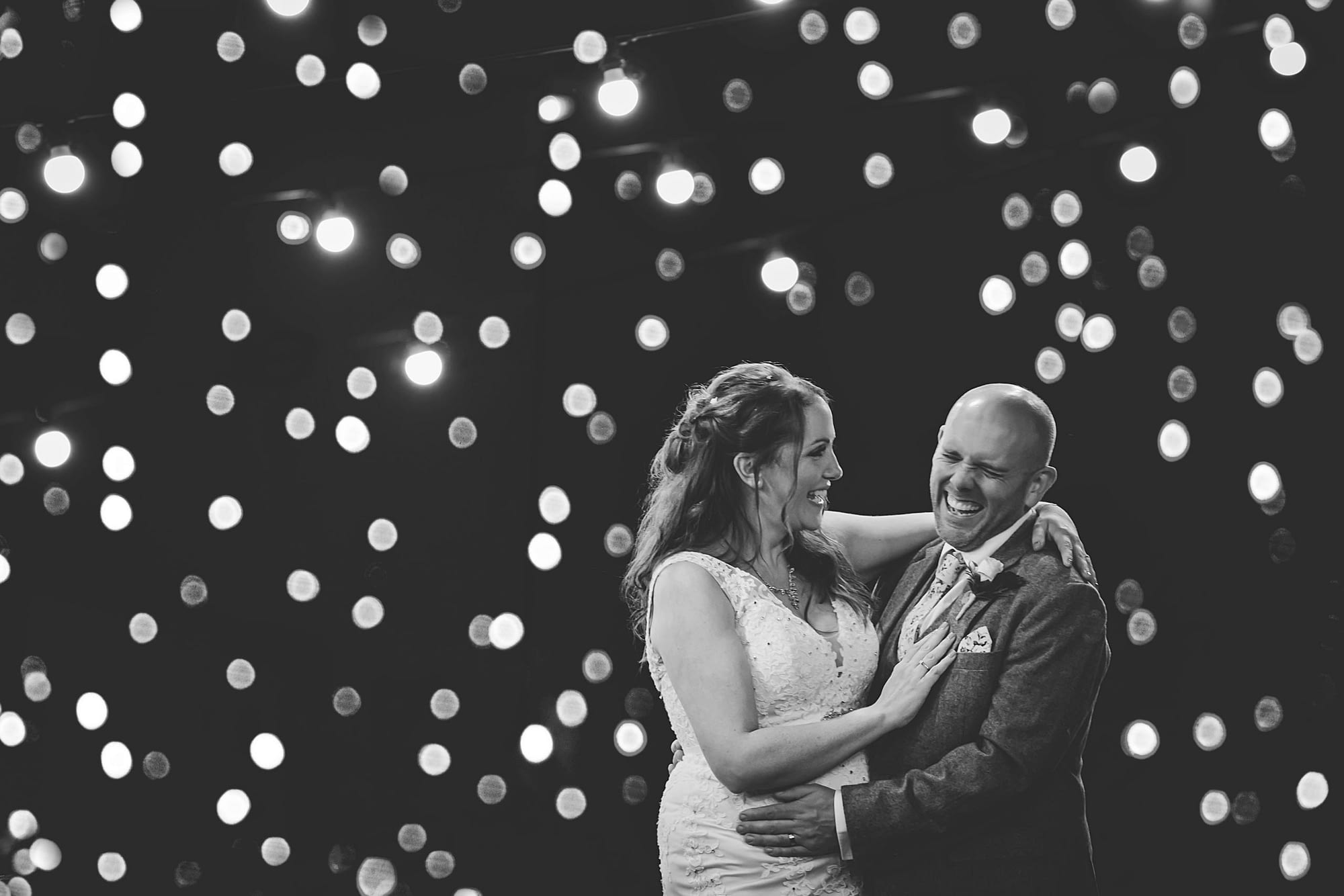 bride and groom laughing at night with twinkling lights in background