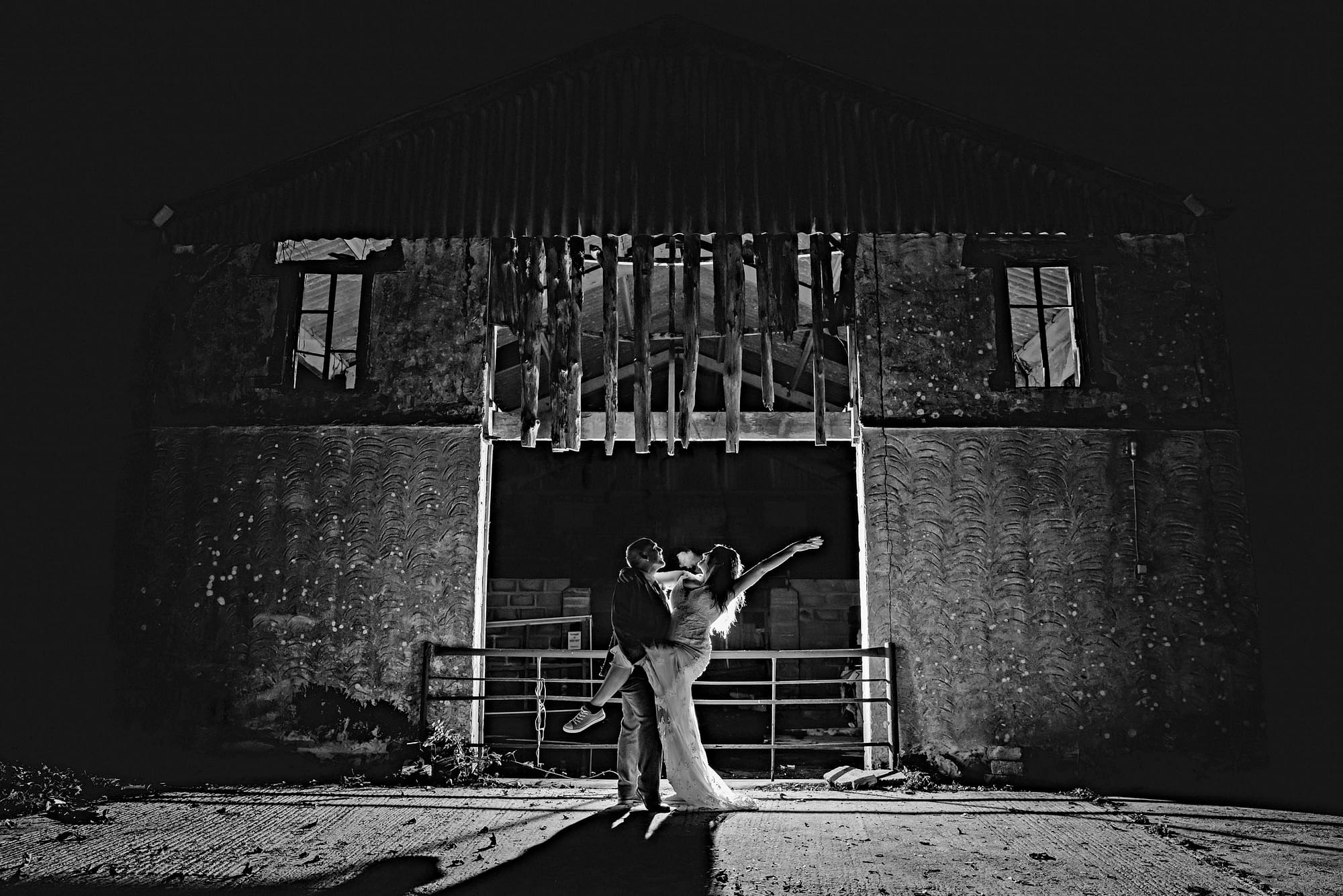 bride and groom dance in front of barn doors at night